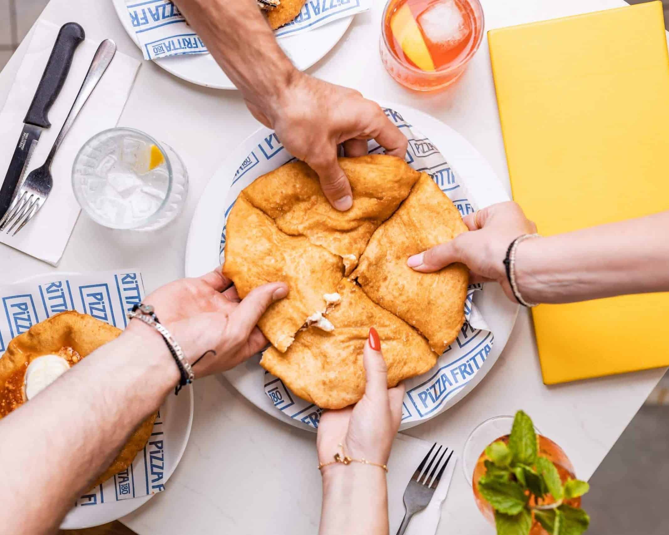 Four people sharing traditional Neapolitan pizza fritta on a plate at an Italian restaurant table with drinks