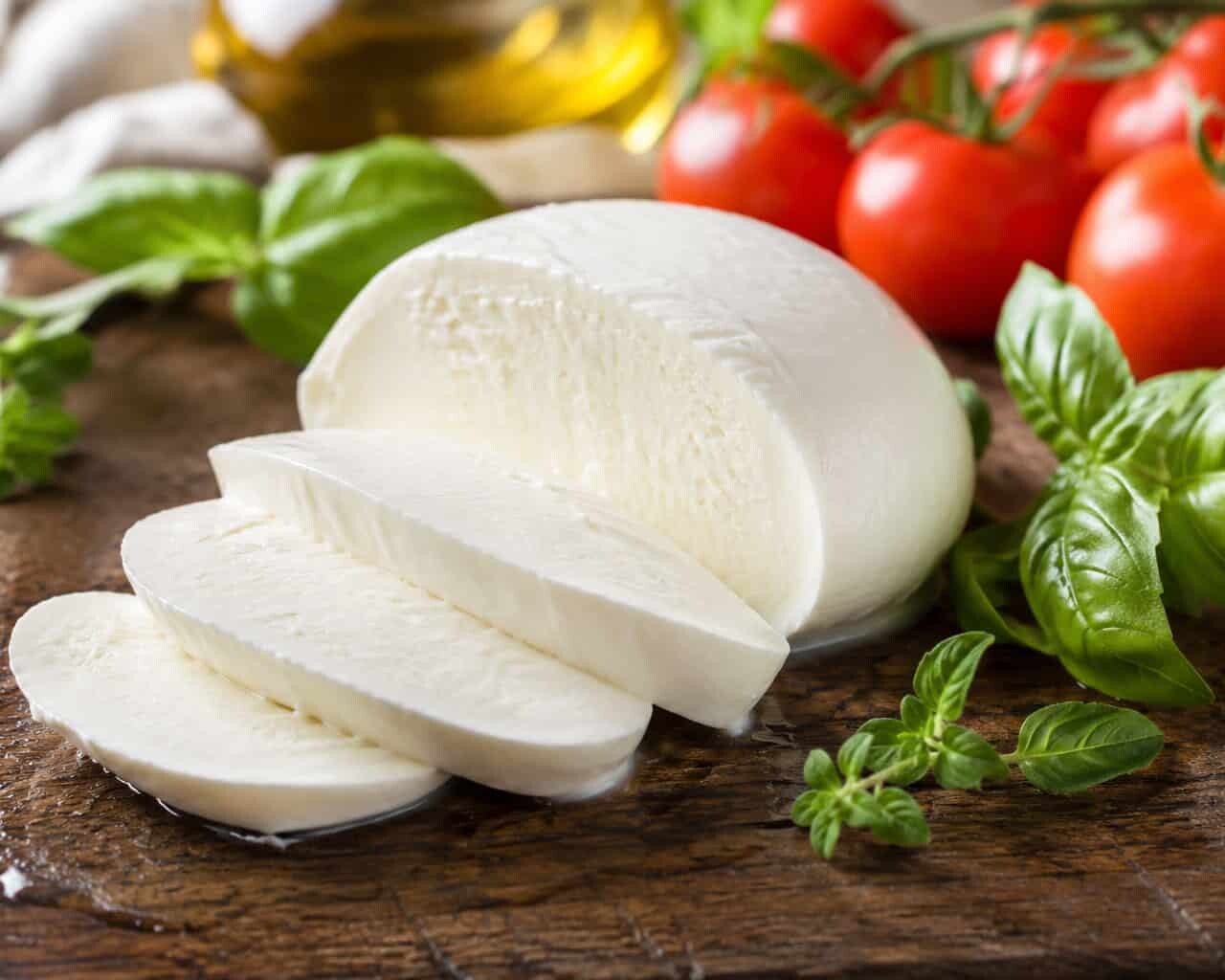 Sliced fior di latte mozzarella (180g) on a wooden board with fresh basil, cherry tomatoes, and olive oil—ideal for pizza fritta.