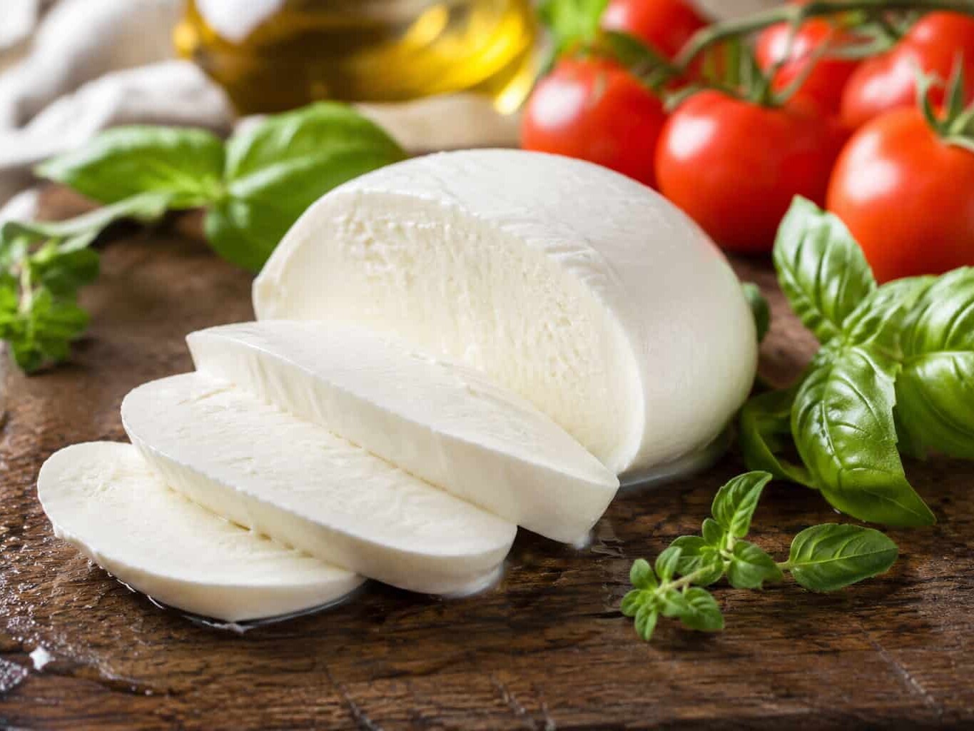 Sliced fior di latte mozzarella (180g) on a wooden board with fresh basil, cherry tomatoes, and olive oil—ideal for pizza fritta.