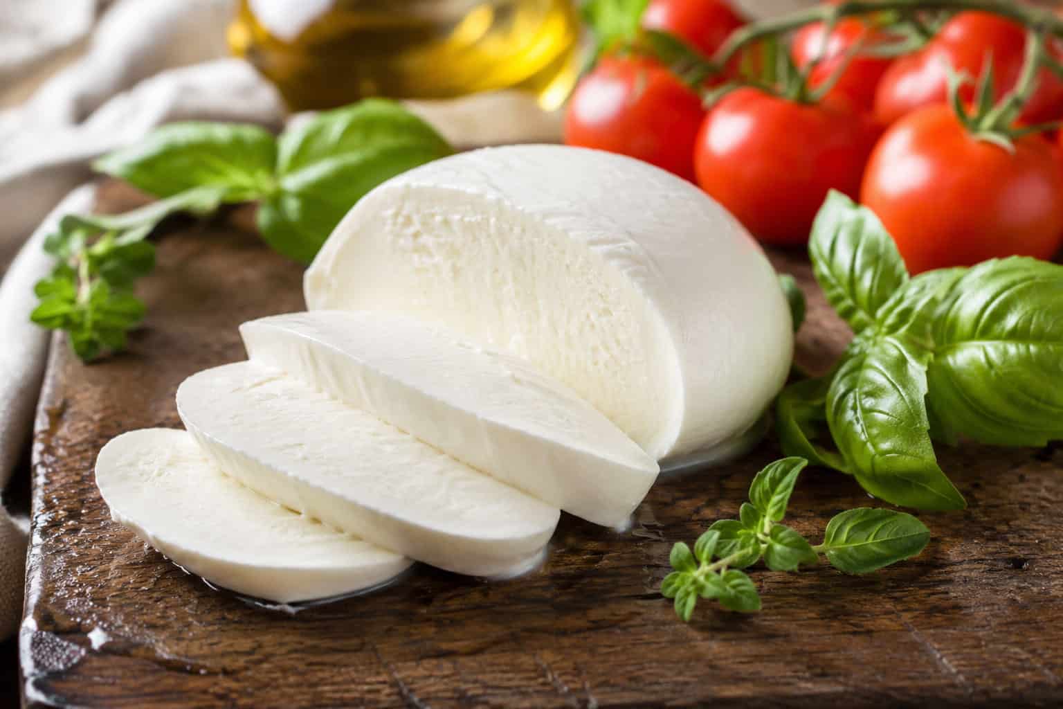 Sliced fior di latte mozzarella (180g) on a wooden board with fresh basil, cherry tomatoes, and olive oil—ideal for pizza fritta.