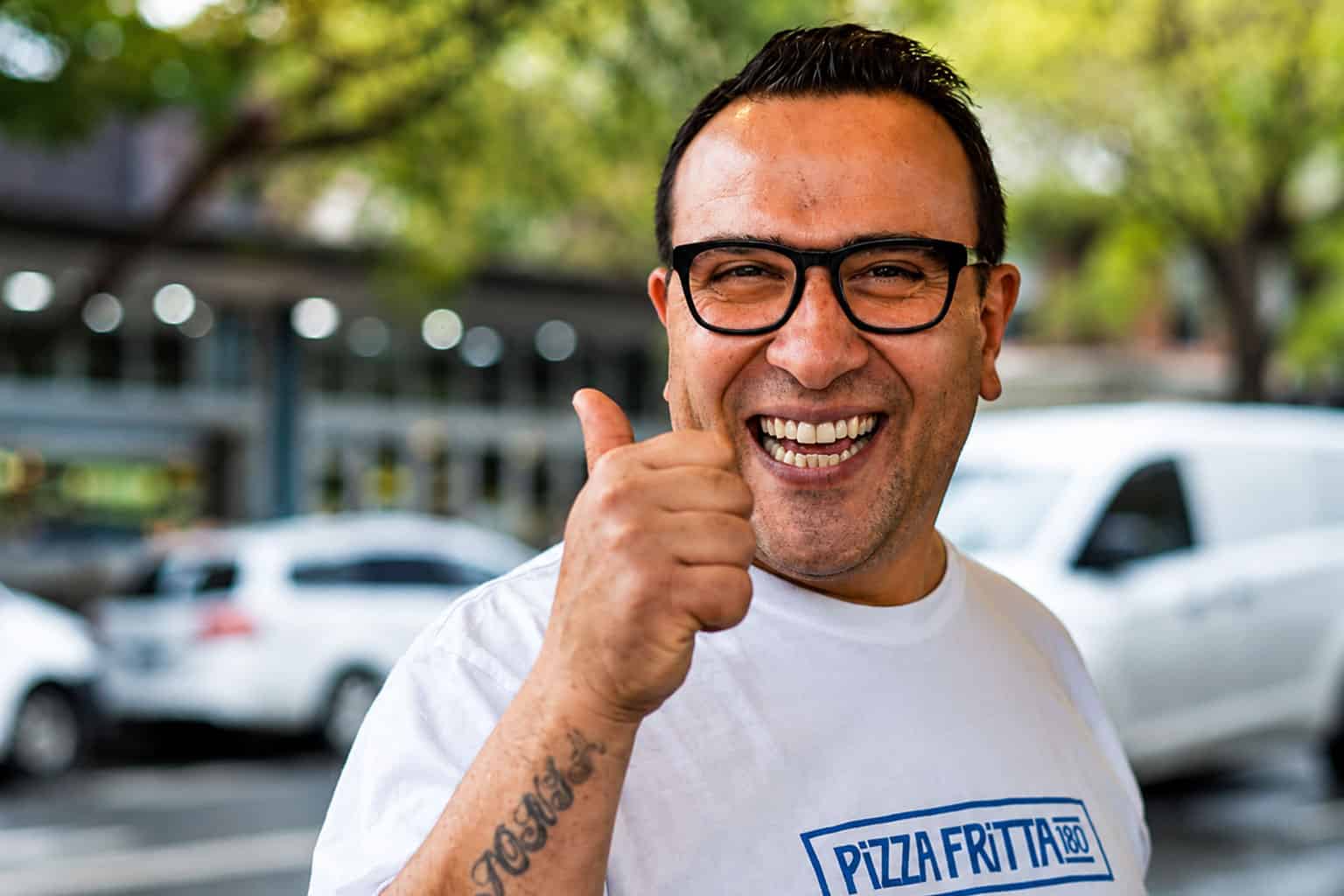 Luigi Esposito, founder of Pizza Fritta 180, giving a thumbs up and smiling outside in a branded white t-shirt.